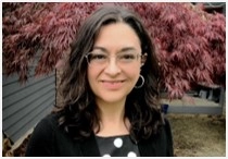 Photo of Dr. Tania May. Woman with brown hair, wearing glasses on and a black outfit.